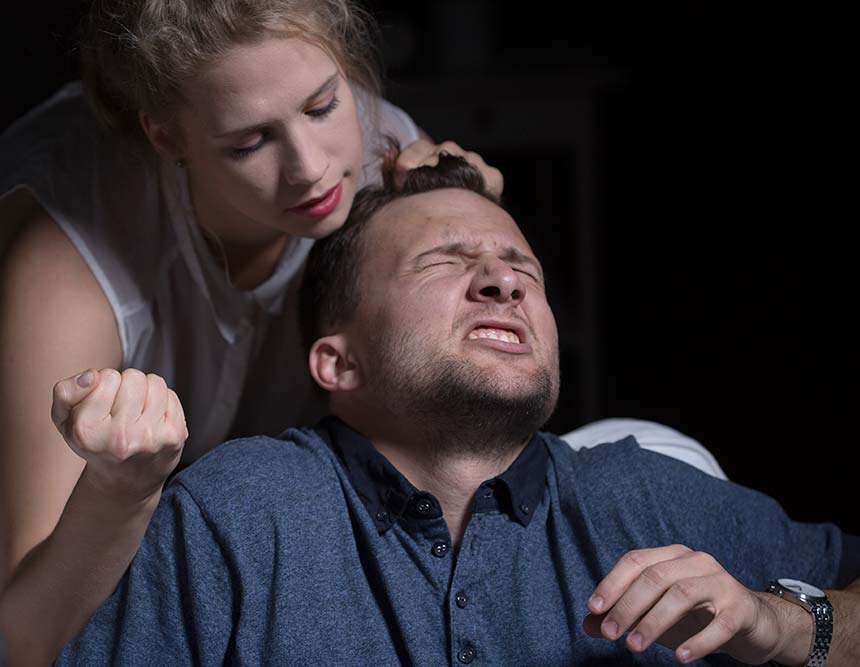 A woman with her hand in a fist is striking a man who looks in pain.